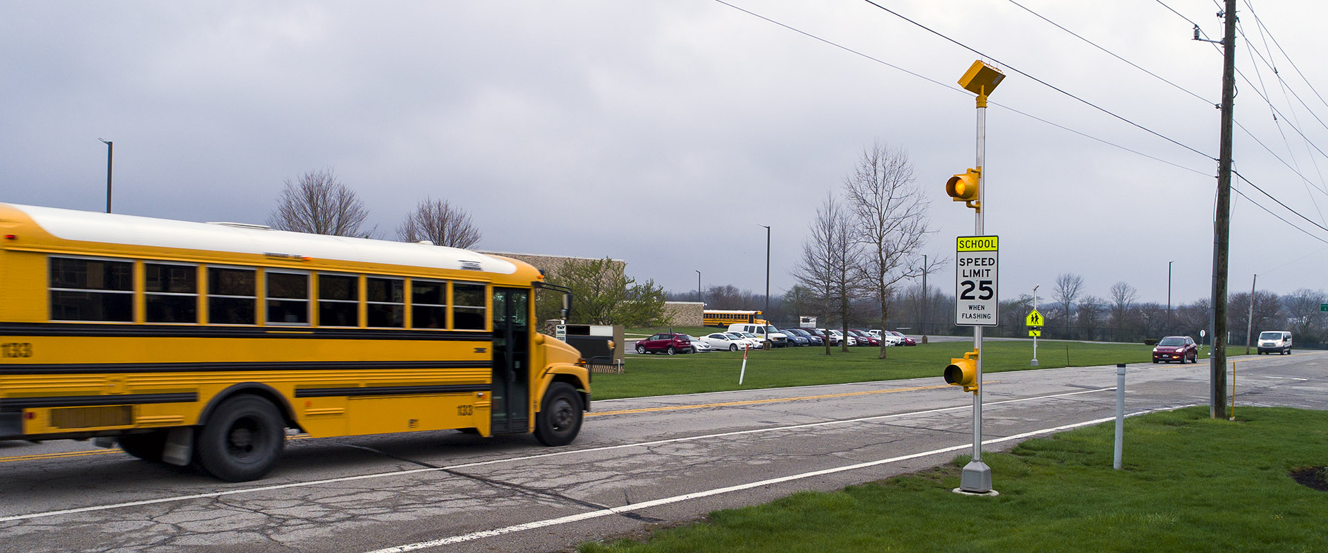 solar-powered school zone traffic beacon with amber flashing light above speed limit sign and school bus