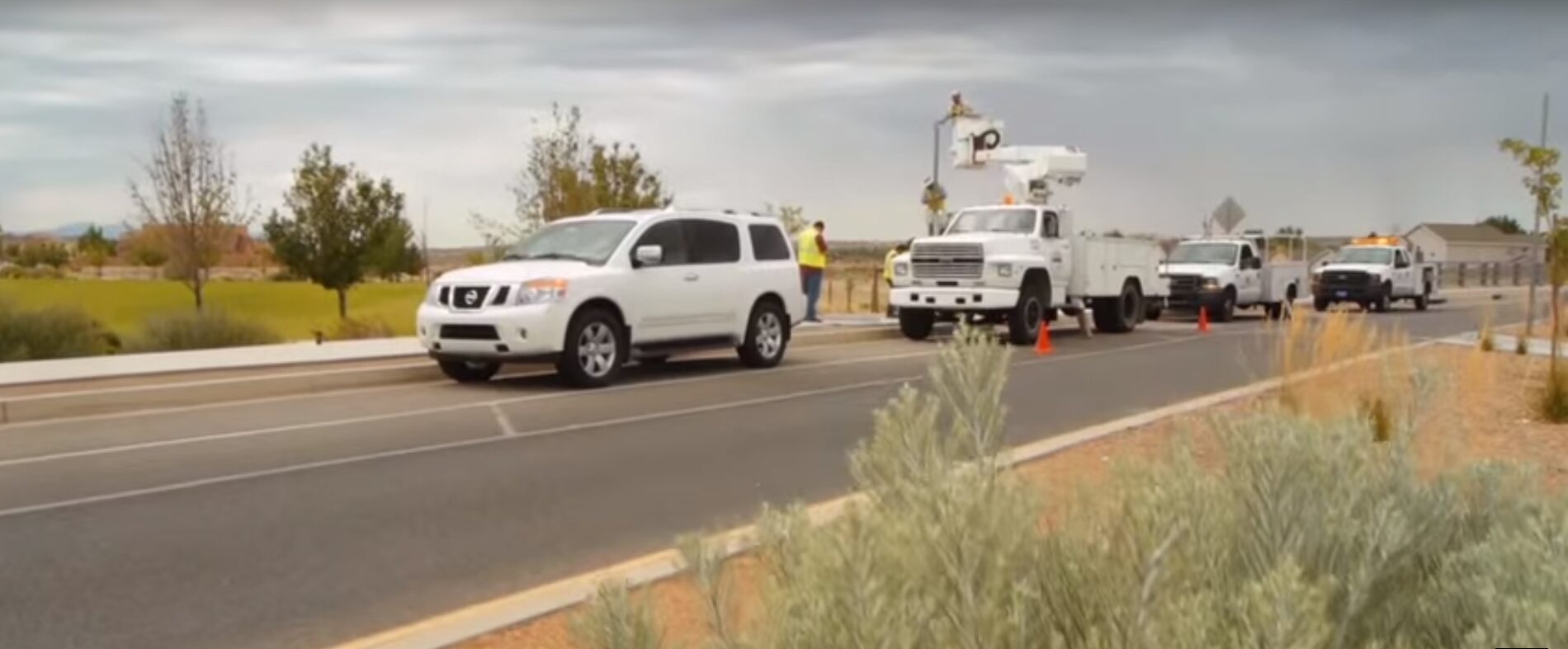 Traffic signal technicians in four utility trucks parked on side of boulevard to install a solar-powered traffic beacon.