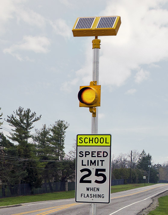 Closeup view of solar-powered school zone traffic beacon with amber flashing light above speed limit sign