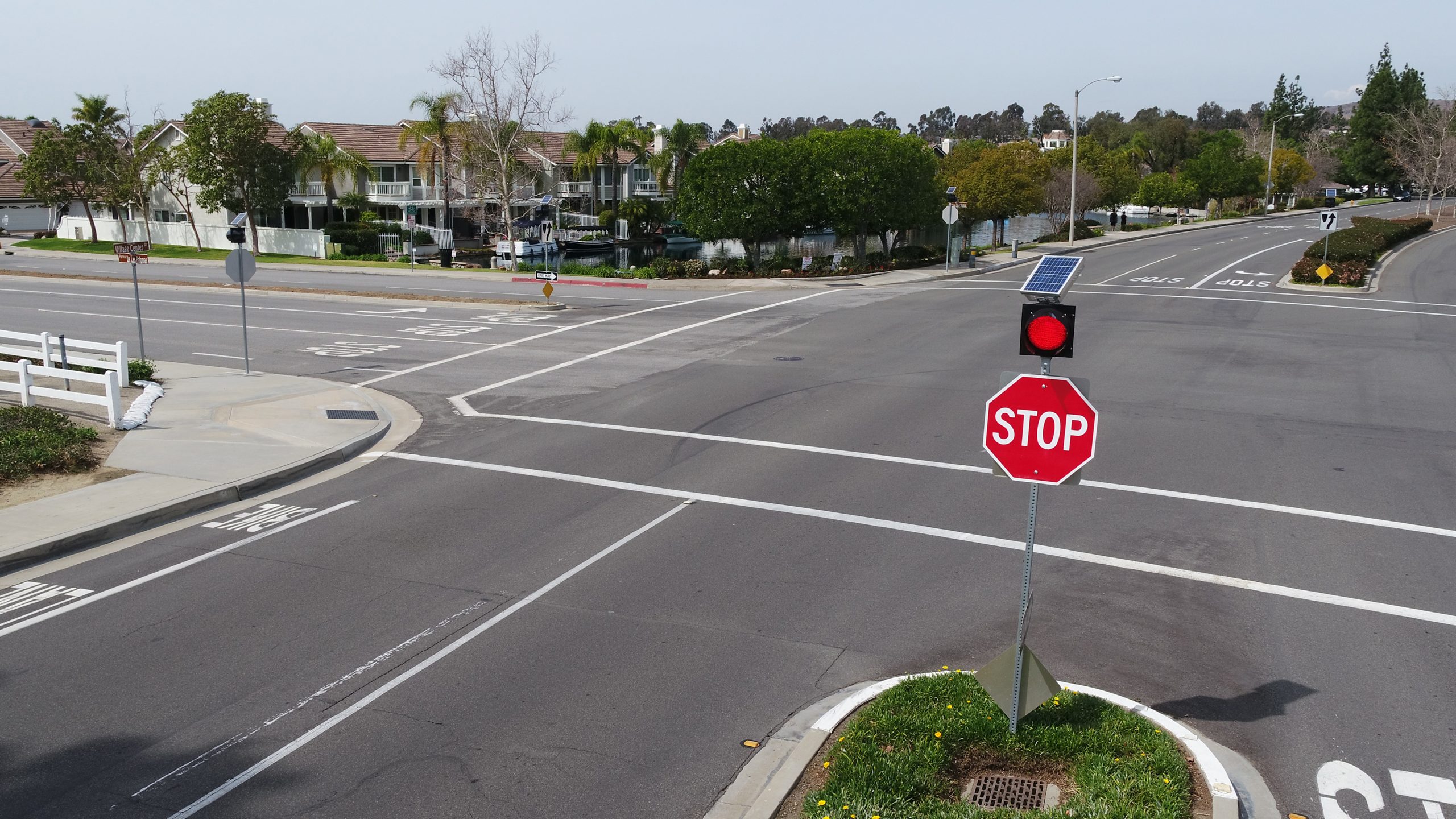 Large street intersection with a stop sign and red flashing light with a solar panel mounted on a pole.