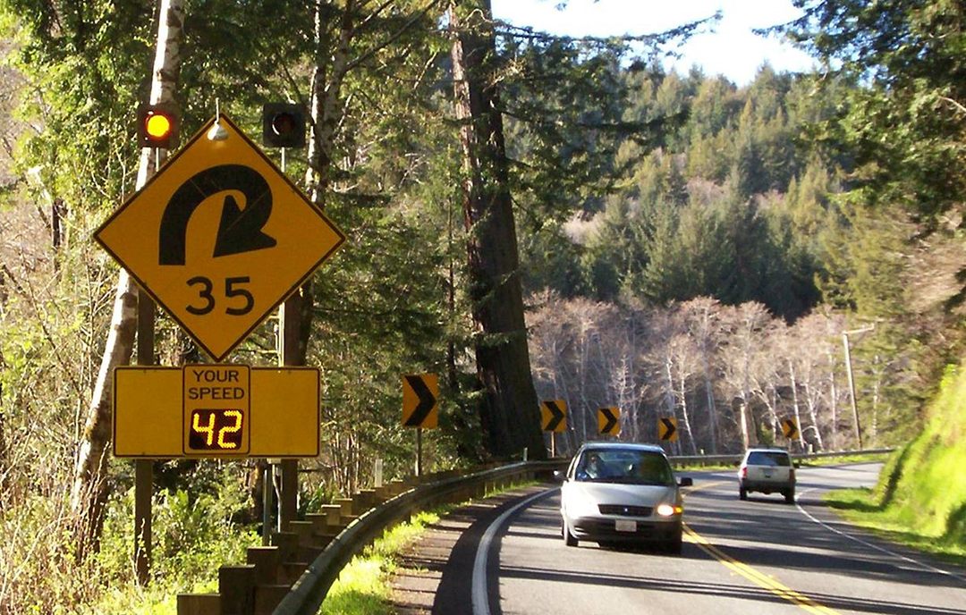 Curved highway with warning sign and flashing lights and your speed radar sign