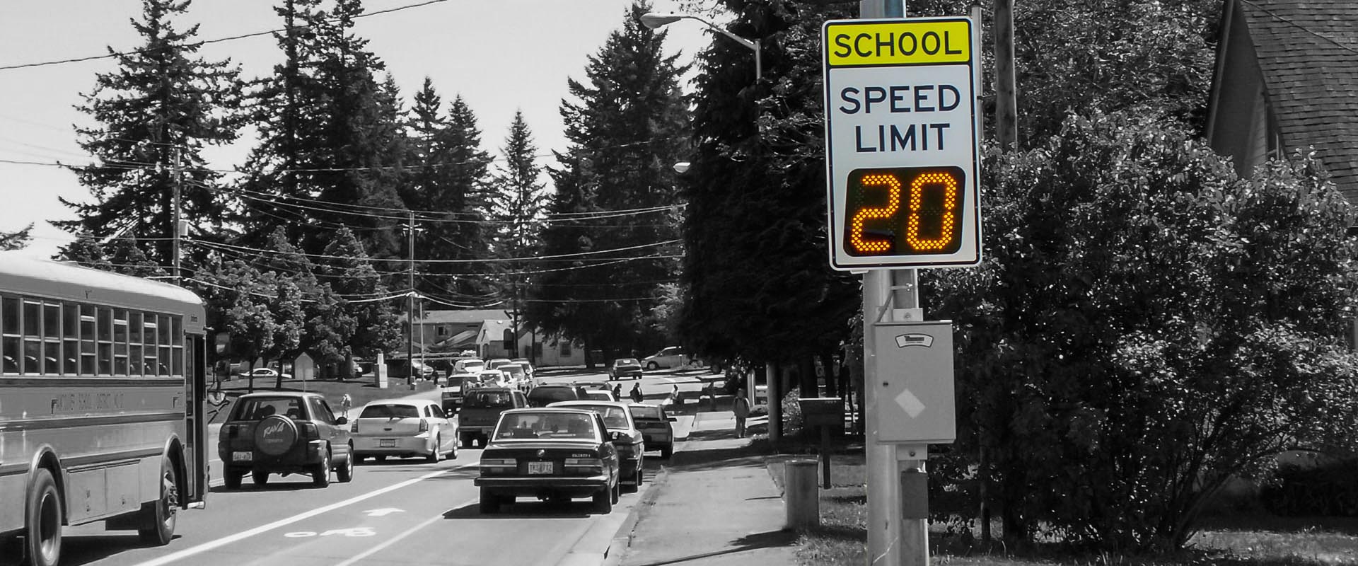 Radar speed sign in school zone with school bus, cars and children walking